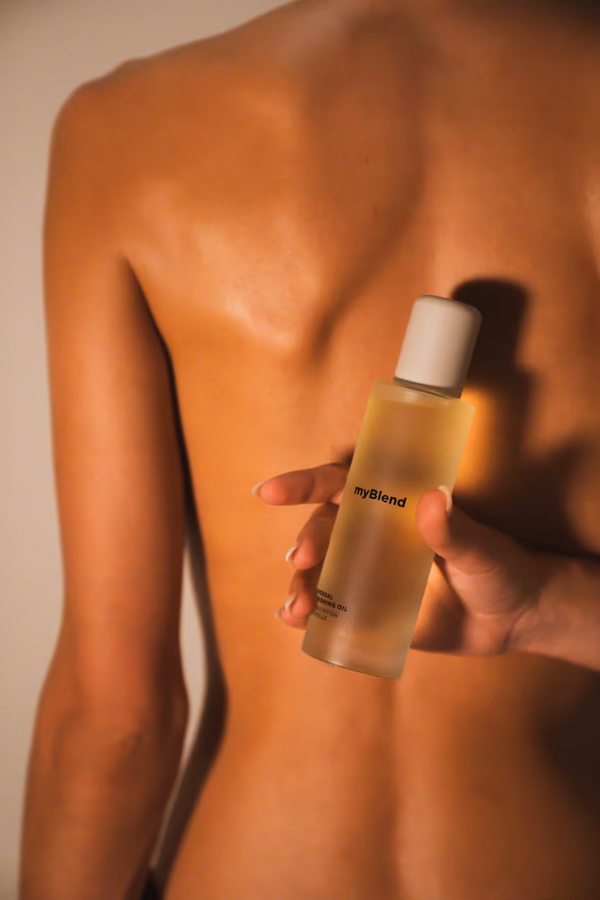 Person nu de dos tenant une bouteille d'huile nourrissante universelle myBlend.