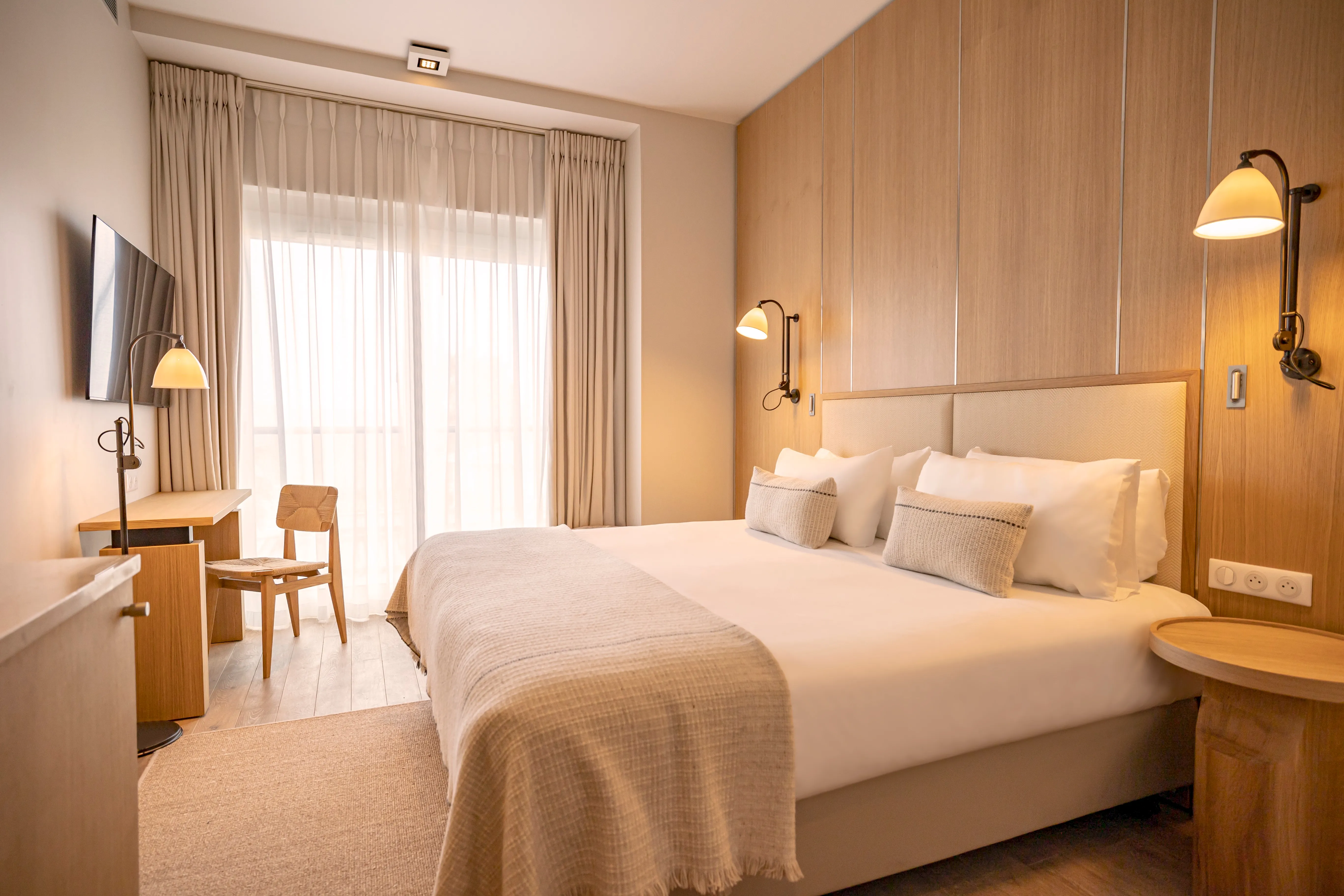 Chambre lumineuse au design naturel avec vue sur mer, rideaux clairs en lin et mobilier en bois chaleureux.
