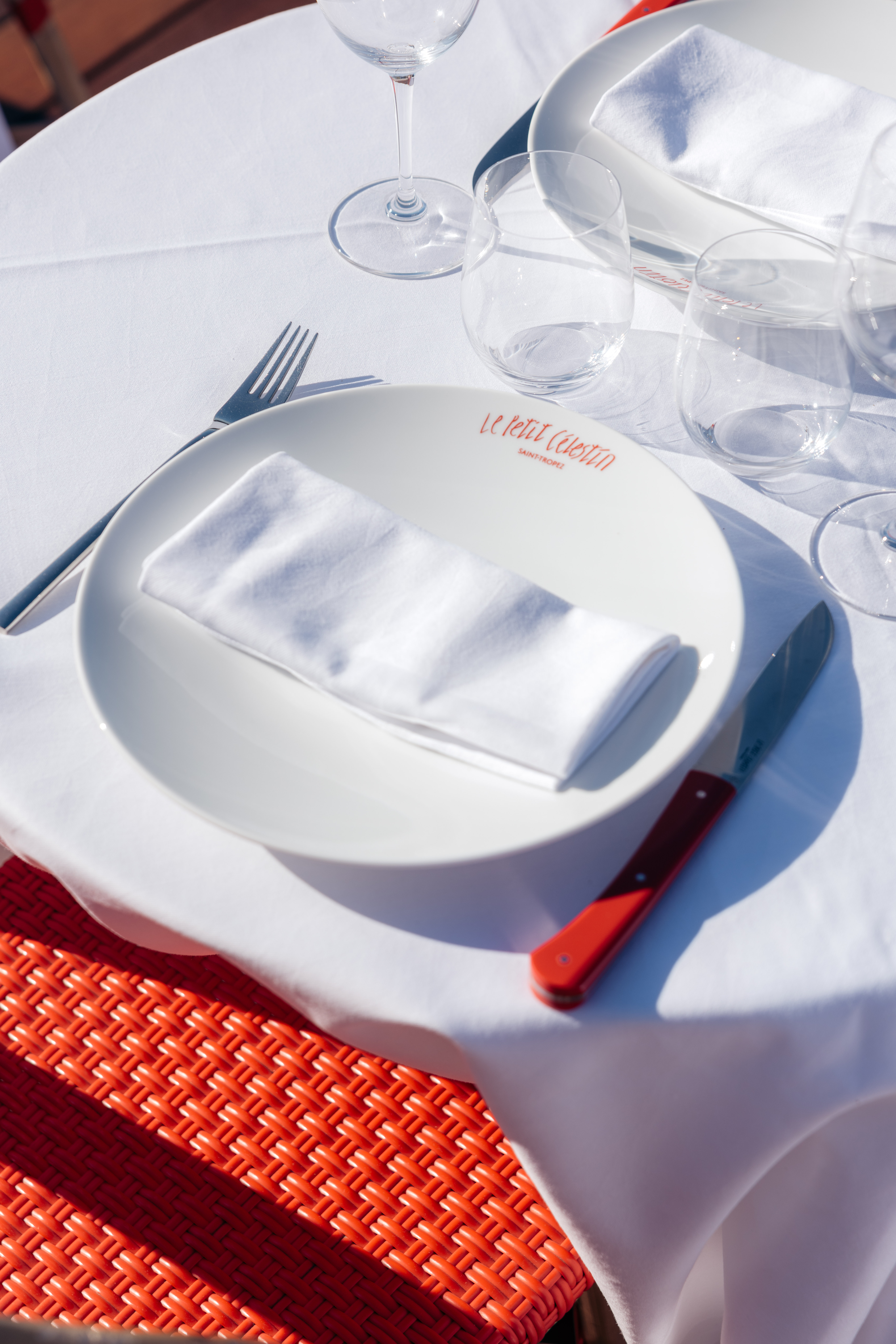 Gros plan sur une table dressée avec assiette blanche et serviette sur une terrasse ensoleillée de restaurant de luxe