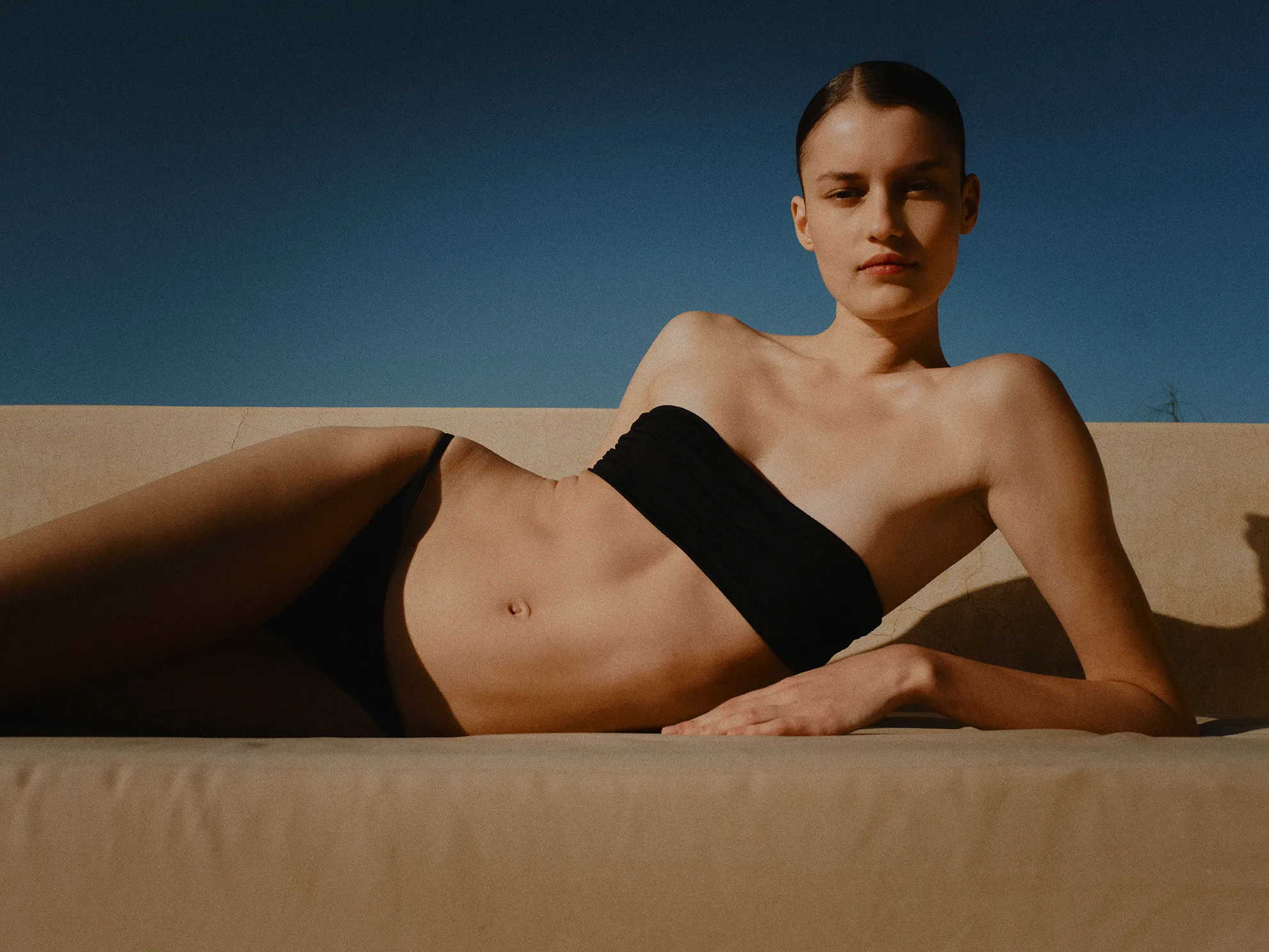 Femme allongée portant un maillot de bain deux pièces noir asymétrique Vanessa Sposi.